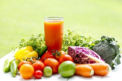 野菜や果物の間にグラスに入ったオレンジ色の野菜ジュース